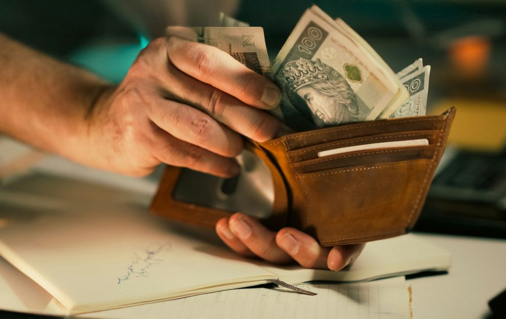 Hands holding us dollar bills in a brown leather wallet