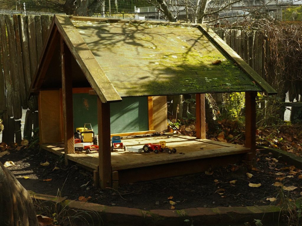 A small wooden playhouse with a chalkboard in a backyard.