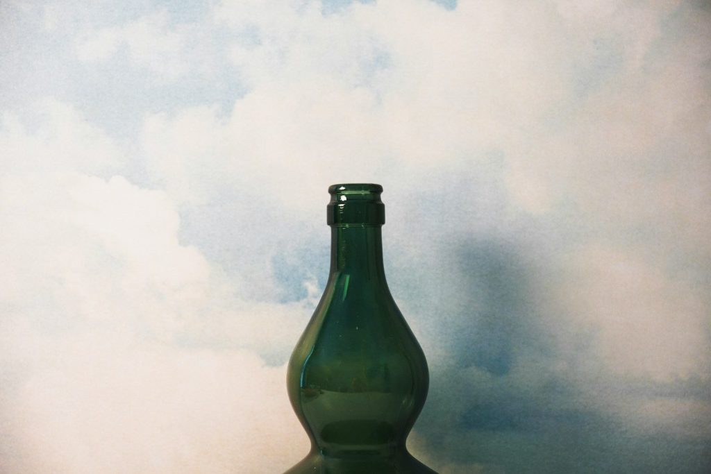 A green bottle stands before a cloudy sky.