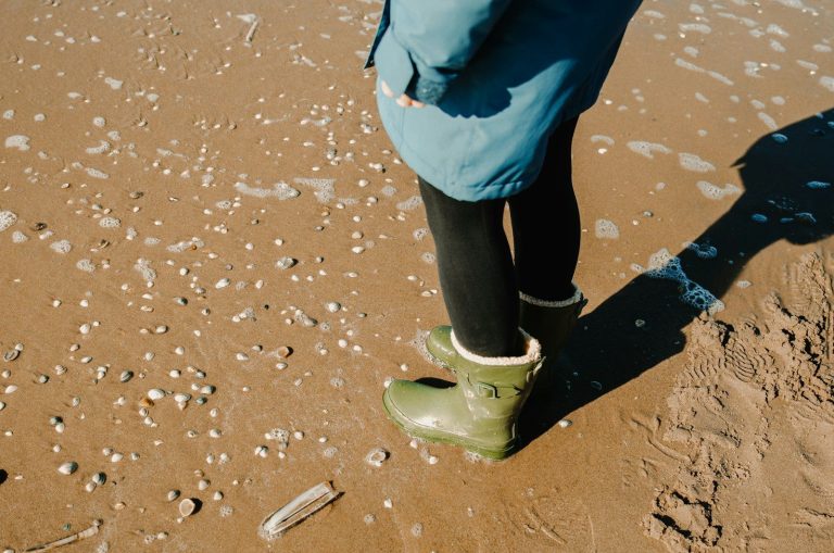 Person stands on a beach in boots.