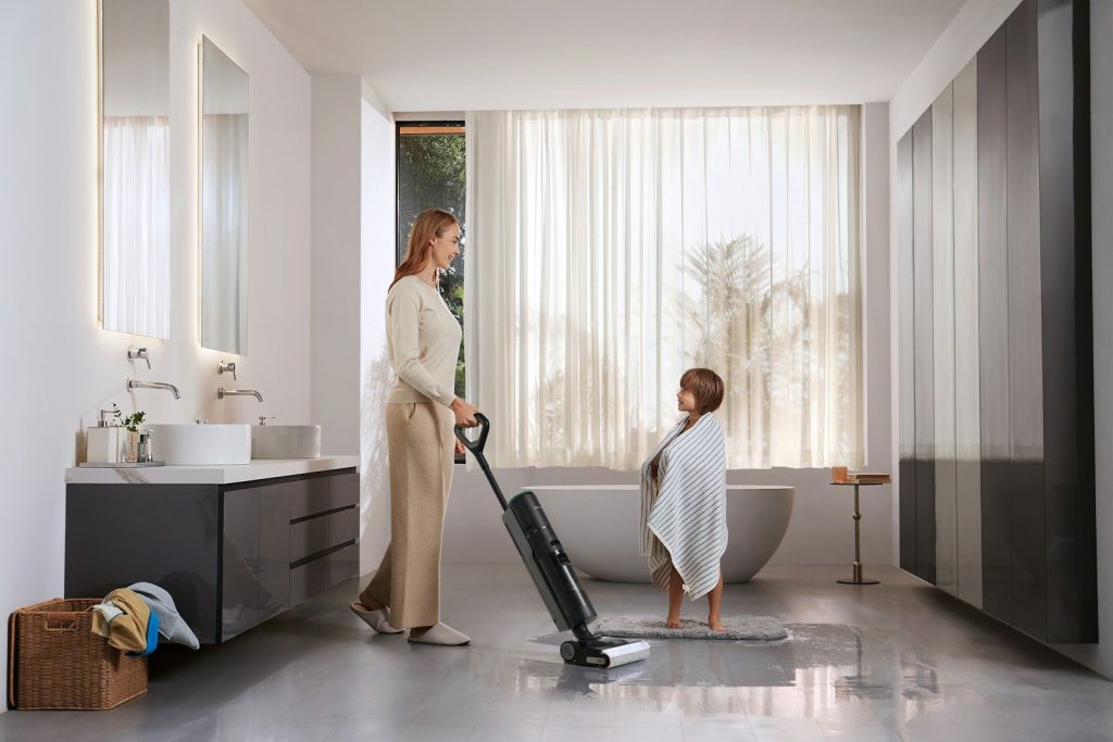 Woman vacuums bathroom while child watches