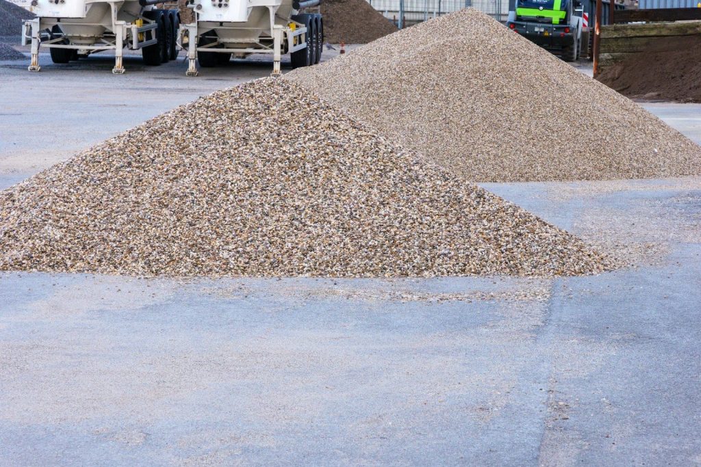 Two large piles of light-colored gravel on concrete pavement.