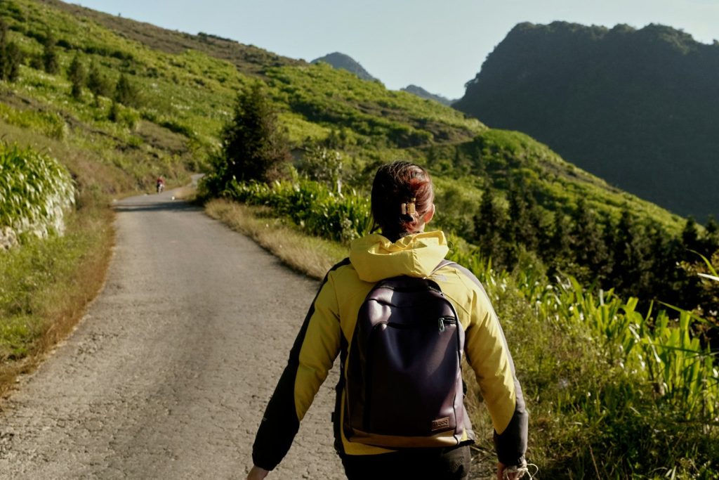 A person walks down a rural road through green hills.