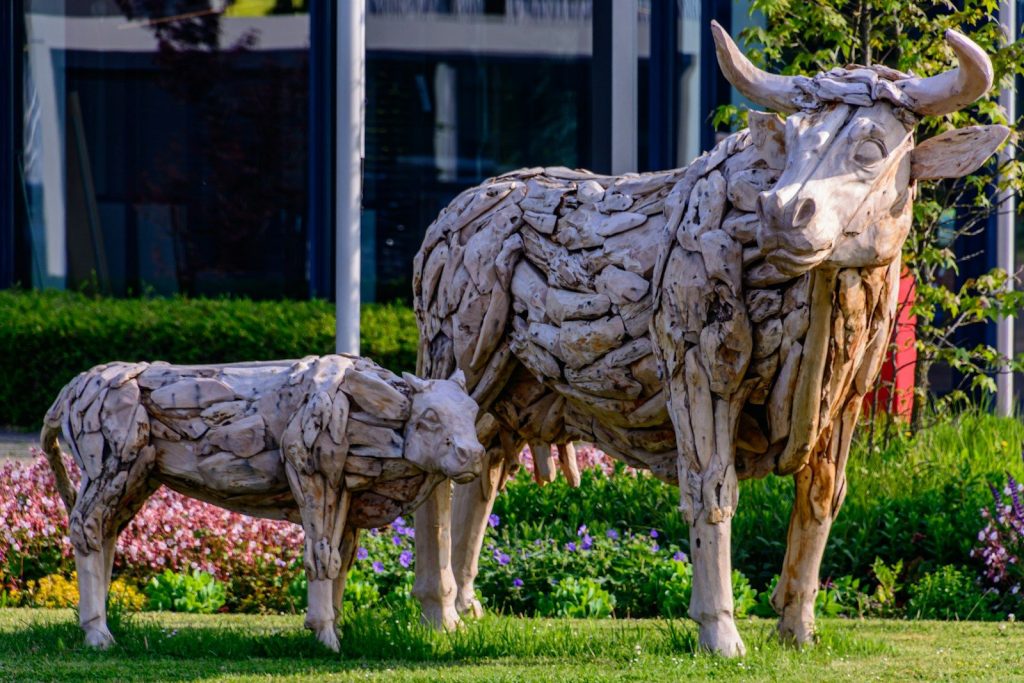 Two wooden cow and calf sculptures on a green lawn.