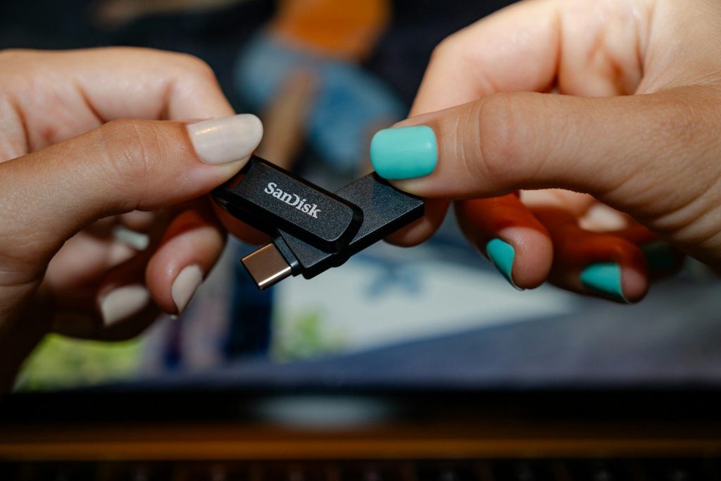 Two hands holding a sandisk usb flash drive.
