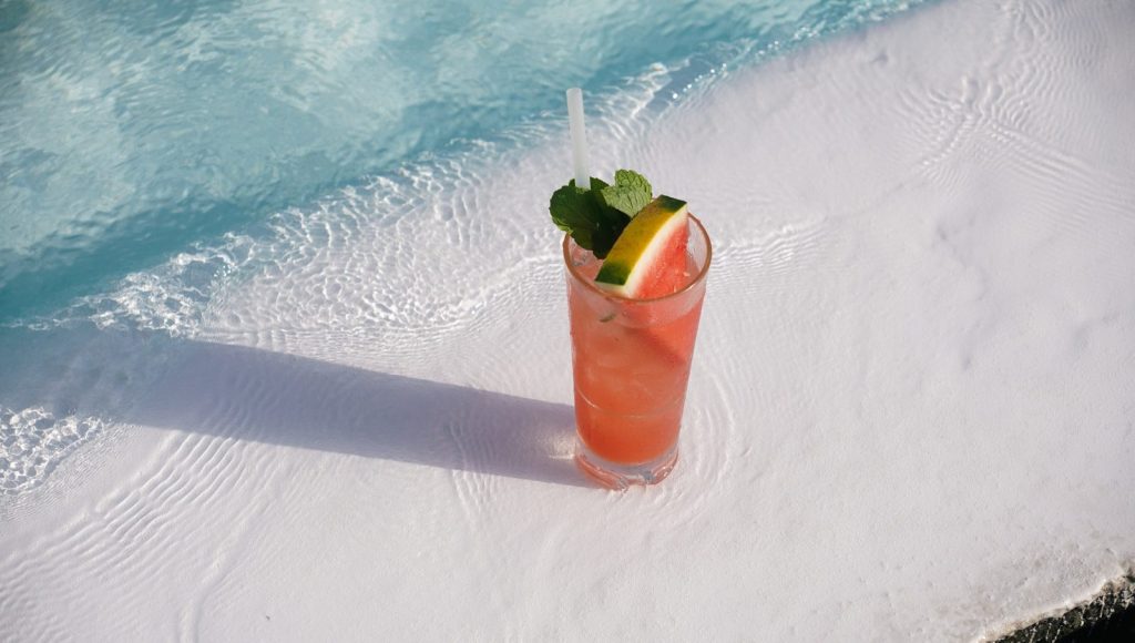 A refreshing pink cocktail with fruit and mint garnish.