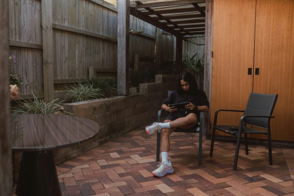 Young woman on patio using tablet in a fenced yard.