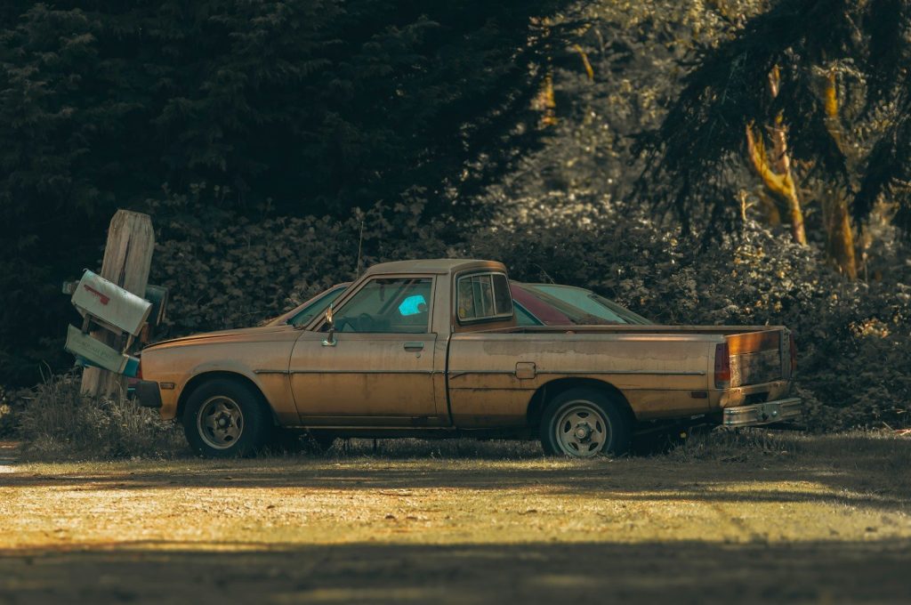 a rusted out car is parked in a field