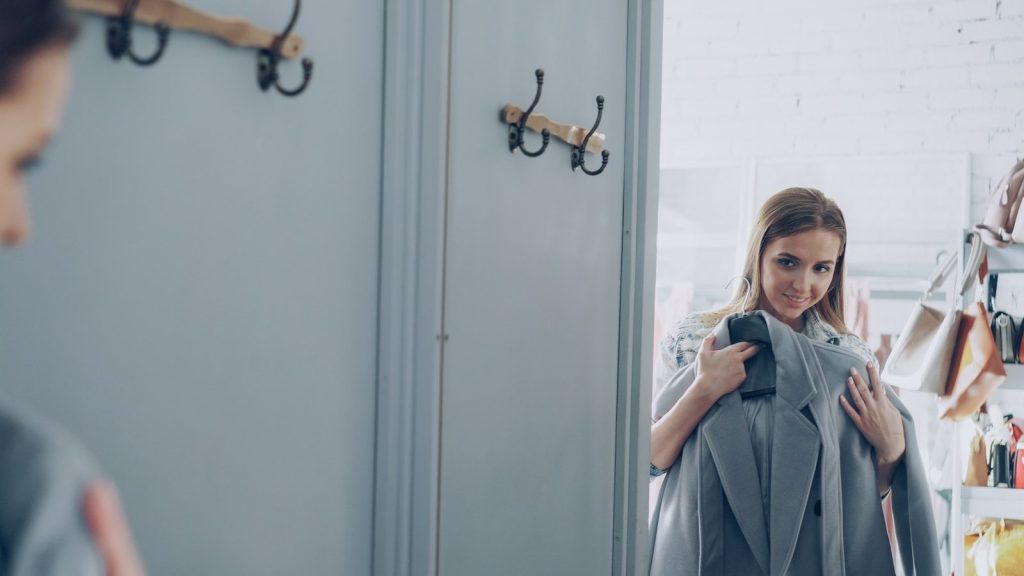 Woman looks in a mirror holding a new coat.