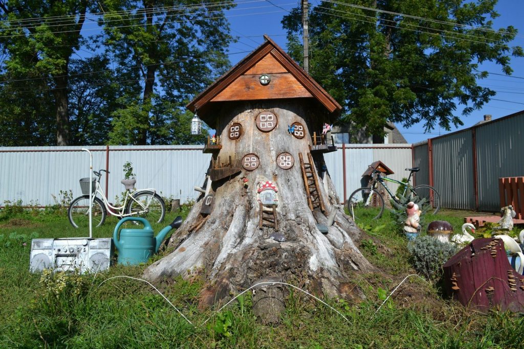 Whimsical tree stump sculpture with surrounding garden decorations.