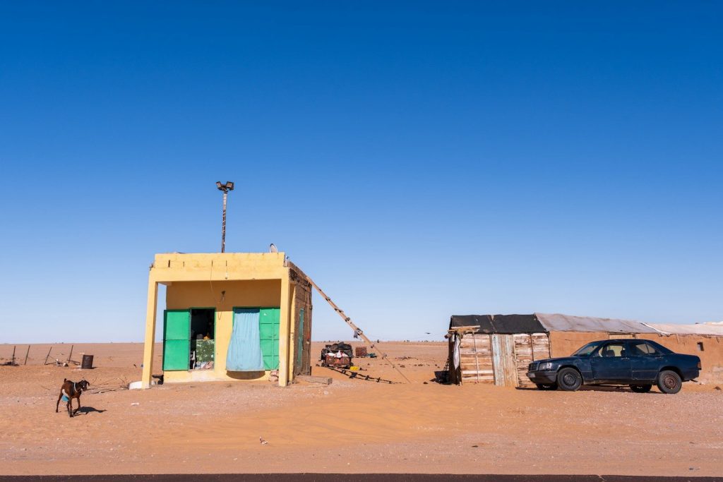 Small buildings, car, and dog in a vast desert landscape.