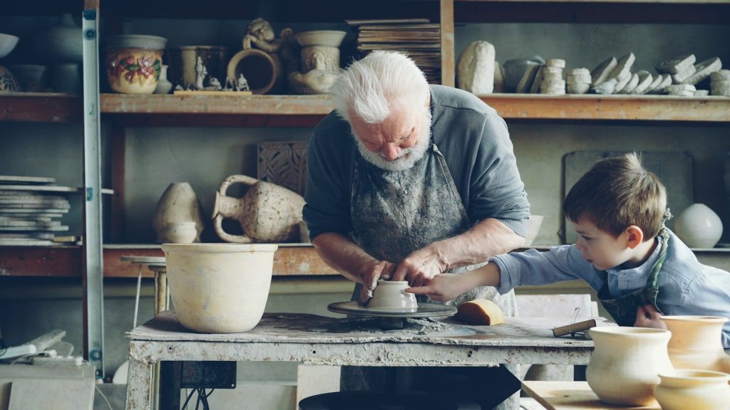 An older potter teaches a child how to mold clay.