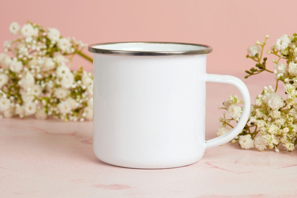 a white mug with a silver rim sitting next to a bunch of white flowers