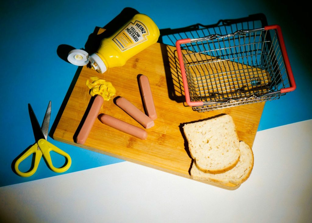 a cutting board with bread, mustard, butter, and a pair of scissors