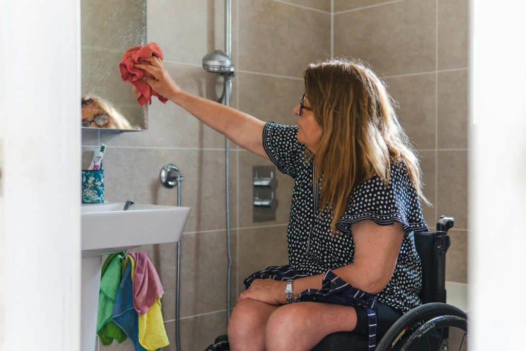 Woman in wheelchair cleaning bathroom mirror
