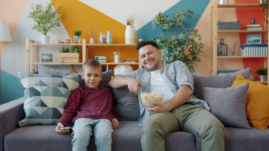 Father and son watching TV with popcorn.