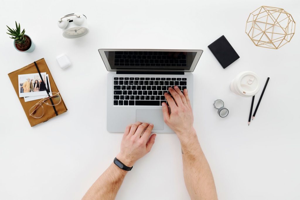 Top view of a minimalist desk layout with a laptop, office supplies, and a person's hands in use.