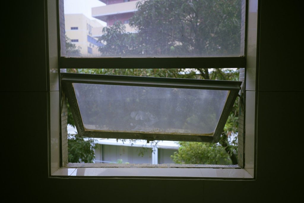 An open window looking out at green trees and buildings.