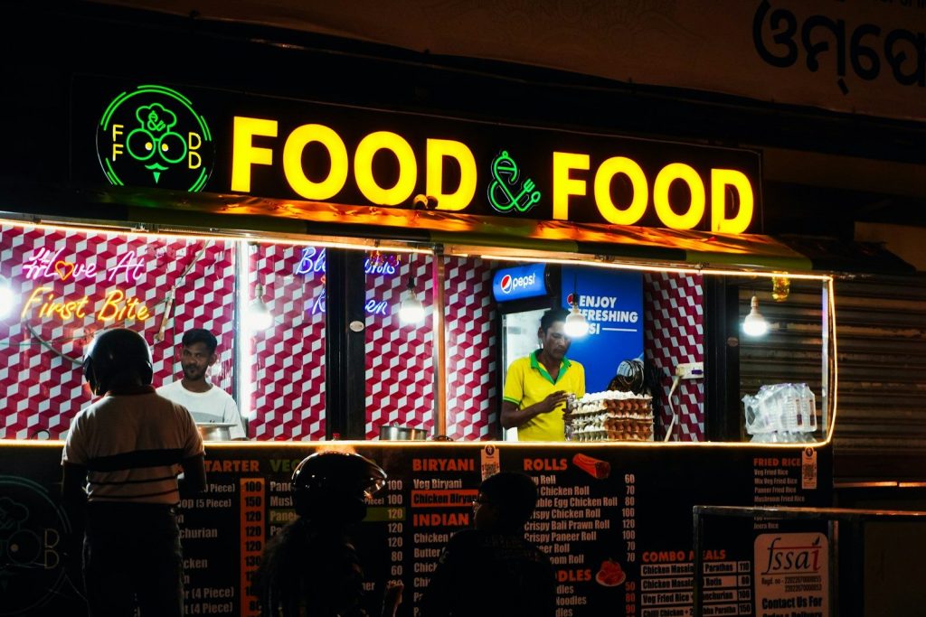 Food stall with bright "food & food" sign at night.