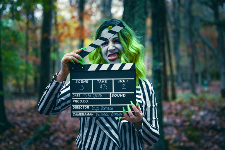 Person in striped costume holding a clapperboard in a forest.