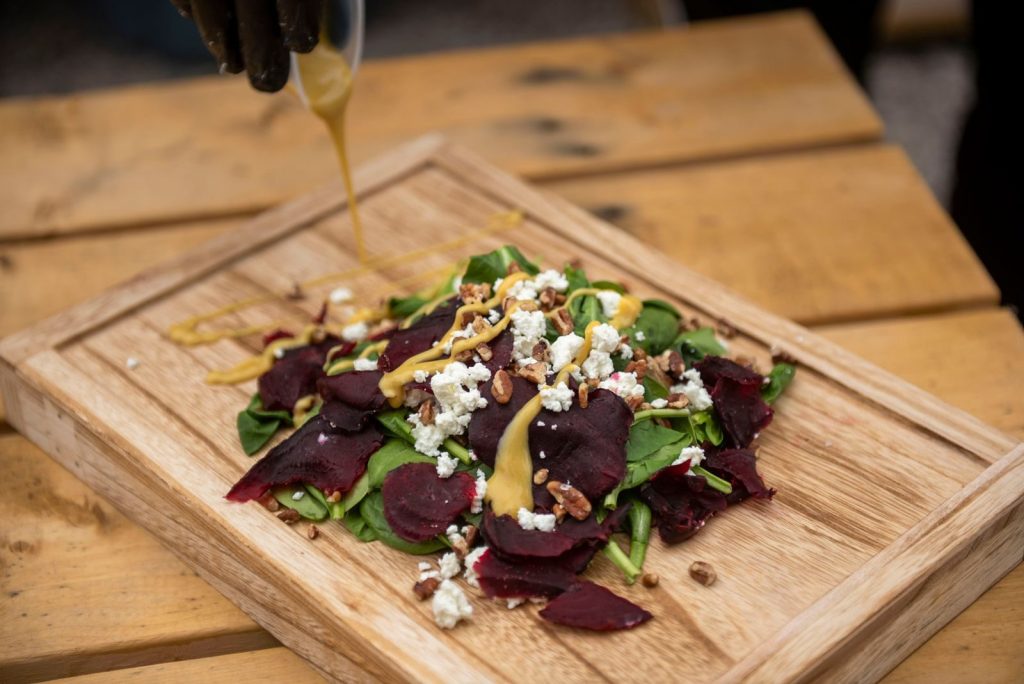 Fresh beetroot salad topped with cheese, dressing, and walnuts on a wooden board.