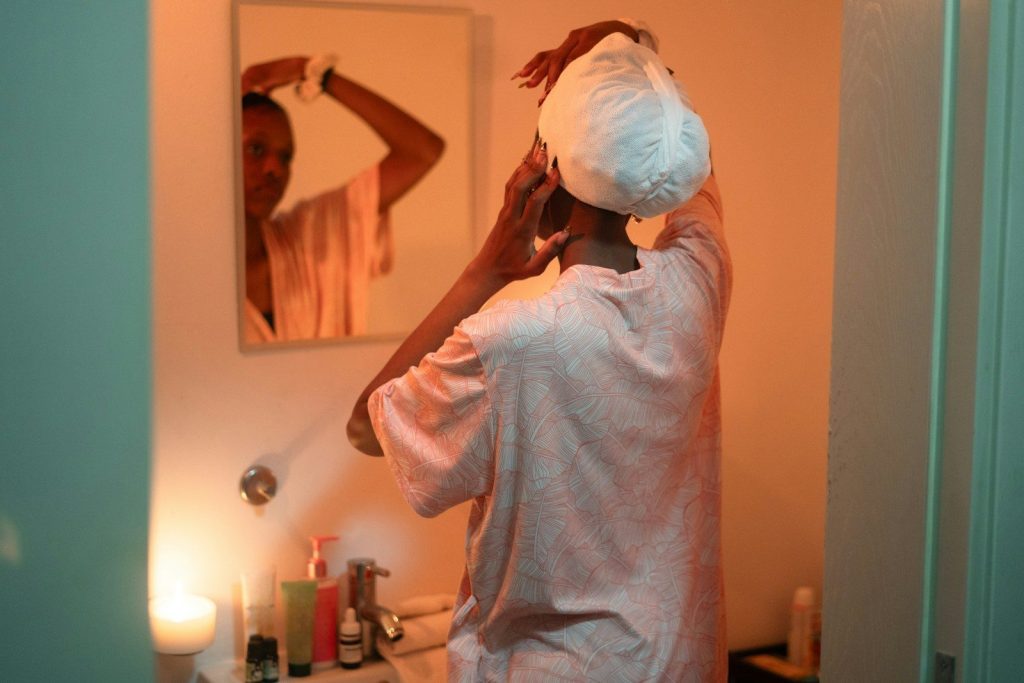 Woman applying towel to hair in bathroom mirror.