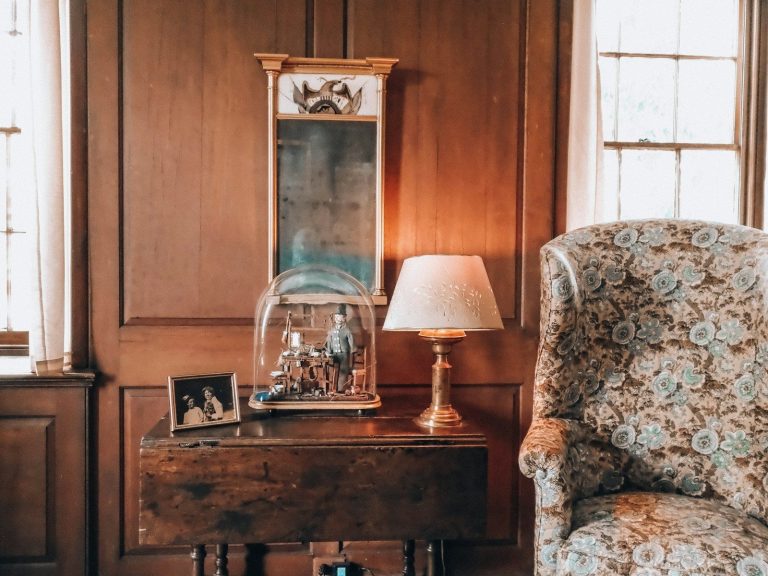 Cozy room with wooden paneling, lamp, mirror, and floral chair.