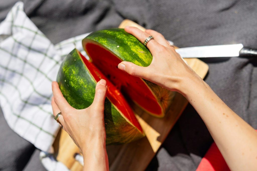 Hands cutting a juicy red watermelon on a cutting board.