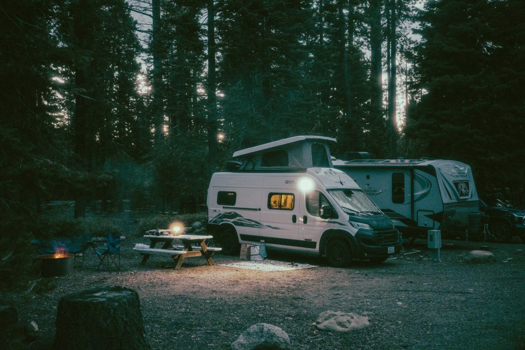 Illuminated camper van and picnic table at a forest campsite.