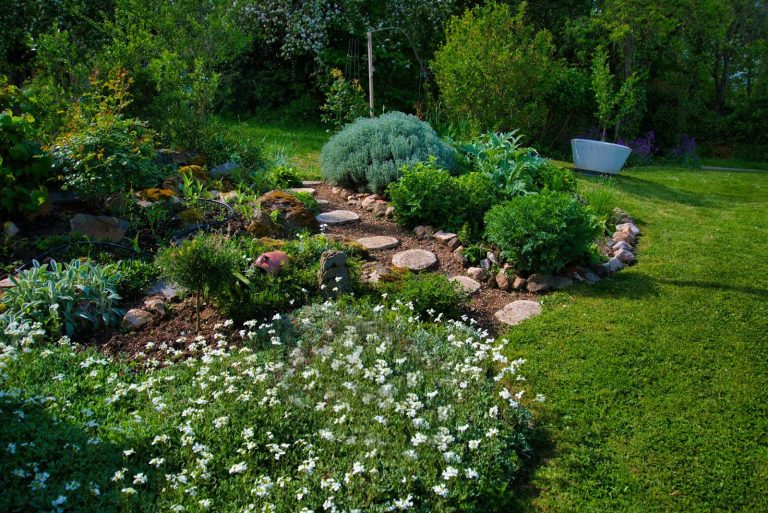 Lush green garden with flowers, plants, and a rock path.