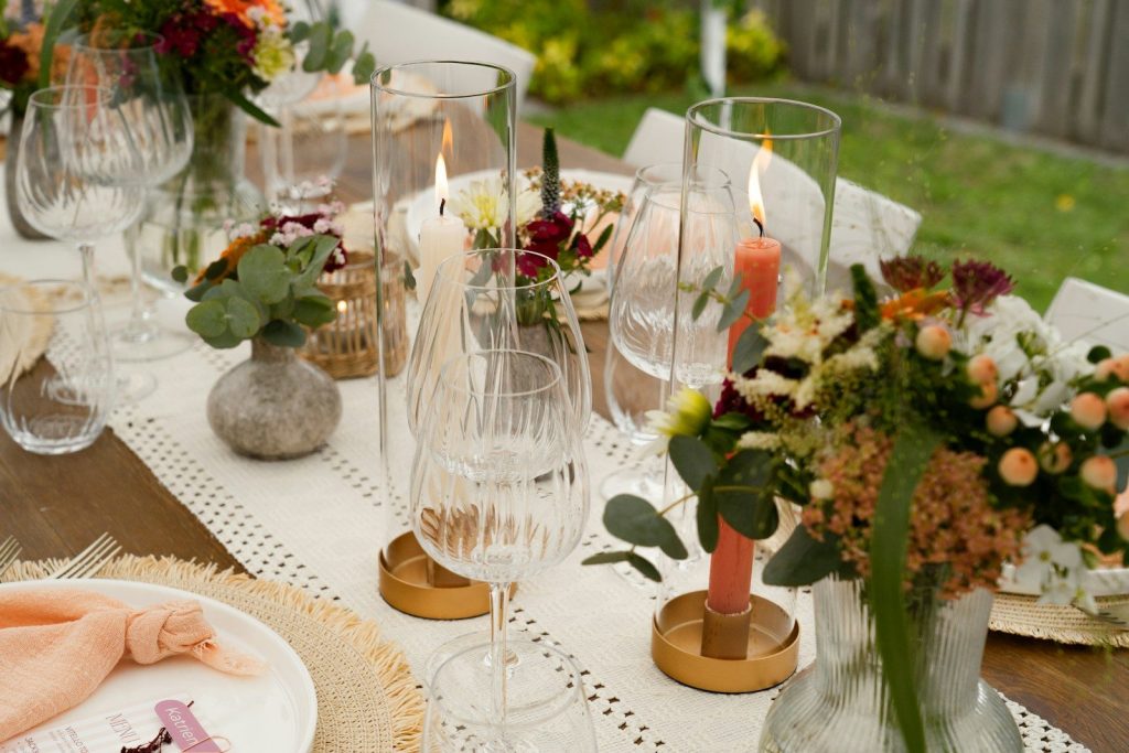 A beautifully decorated outdoor table with flowers, candles, and glassware.