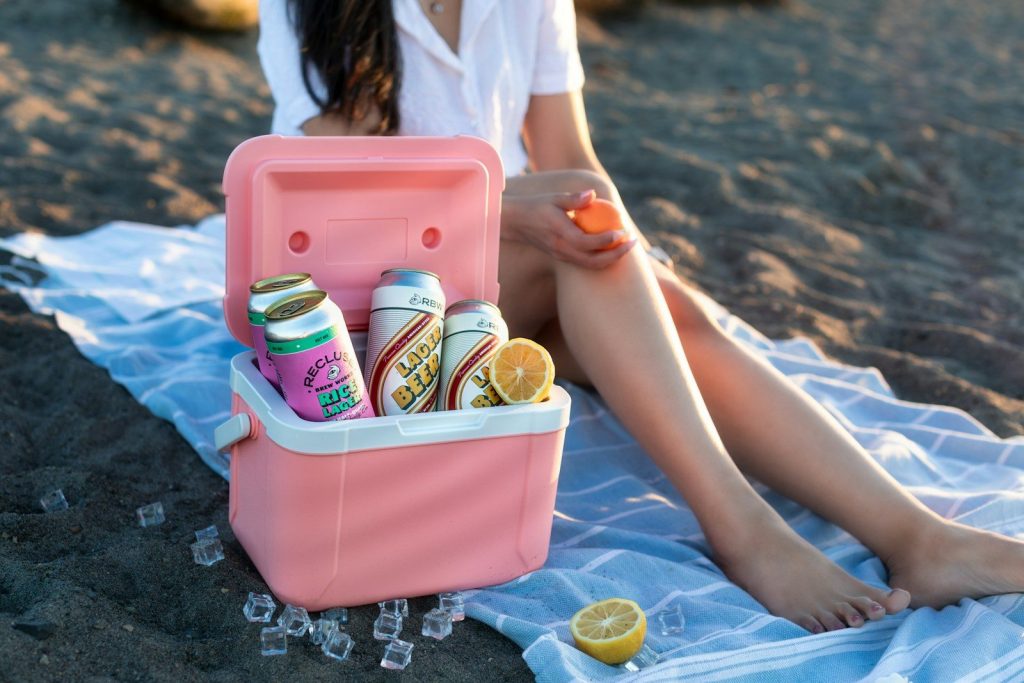 a woman sitting on a towel on the beach with a cooler