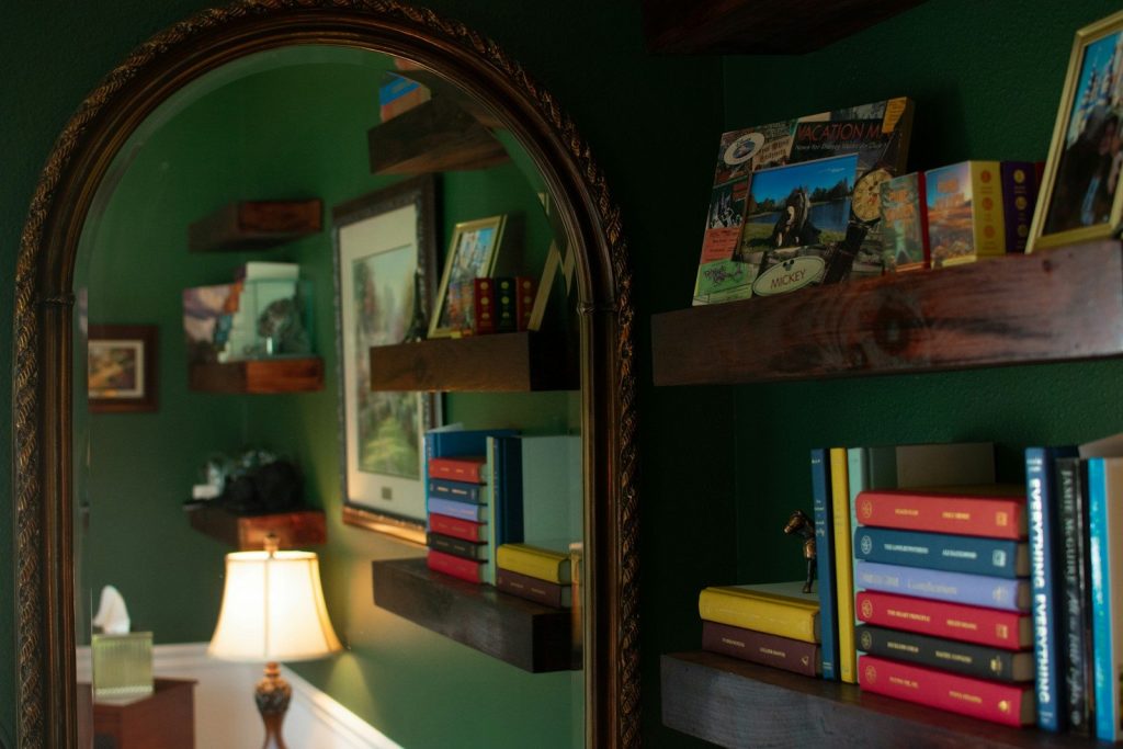 A room with a mirror, bookshelf and a lamp