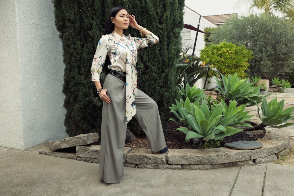 A woman poses in wide-leg pants and a patterned top.