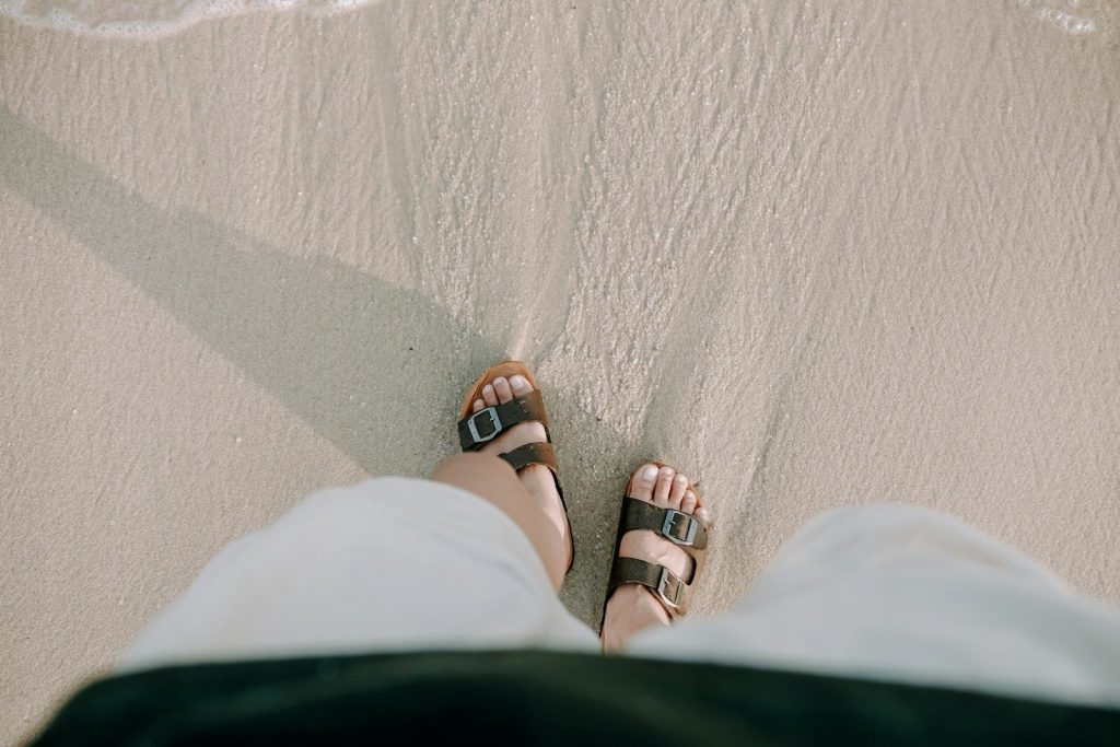 Feet in sandals on a sandy beach near water
