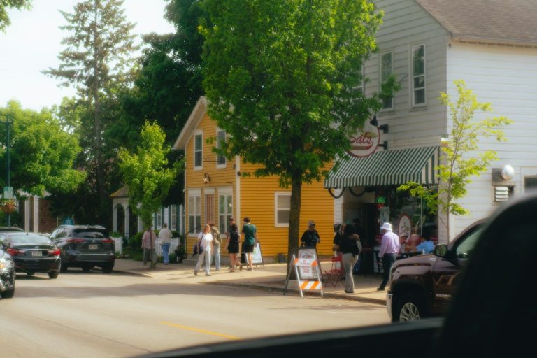 People stroll past a yellow building on a sunny street.