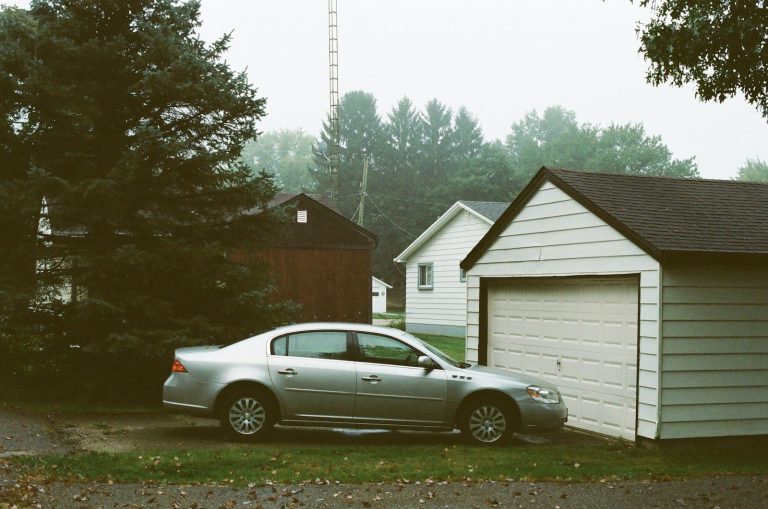 silver sedan parked beside white wooden house during daytime