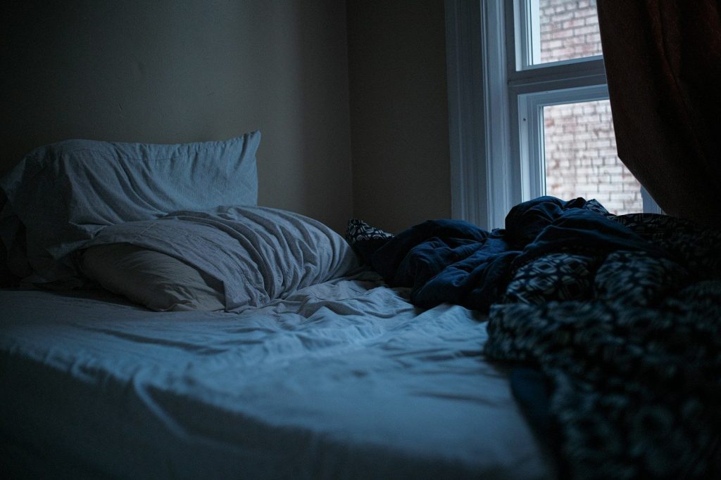 An unmade bed in a dark, quiet bedroom.