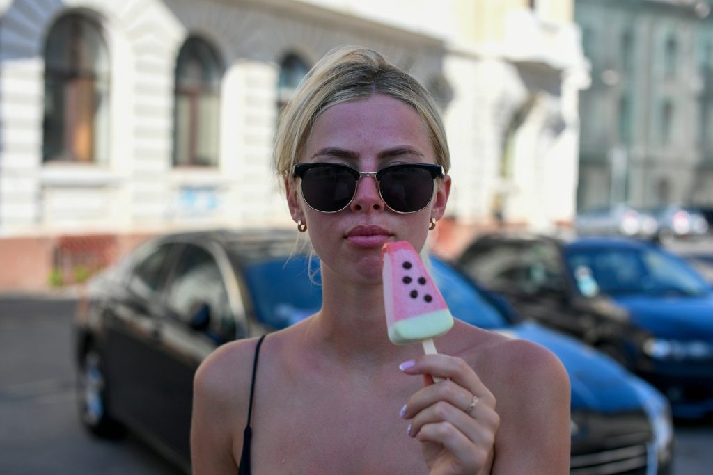 A young woman in sunglasses eating a watermelon popsicle outdoors.