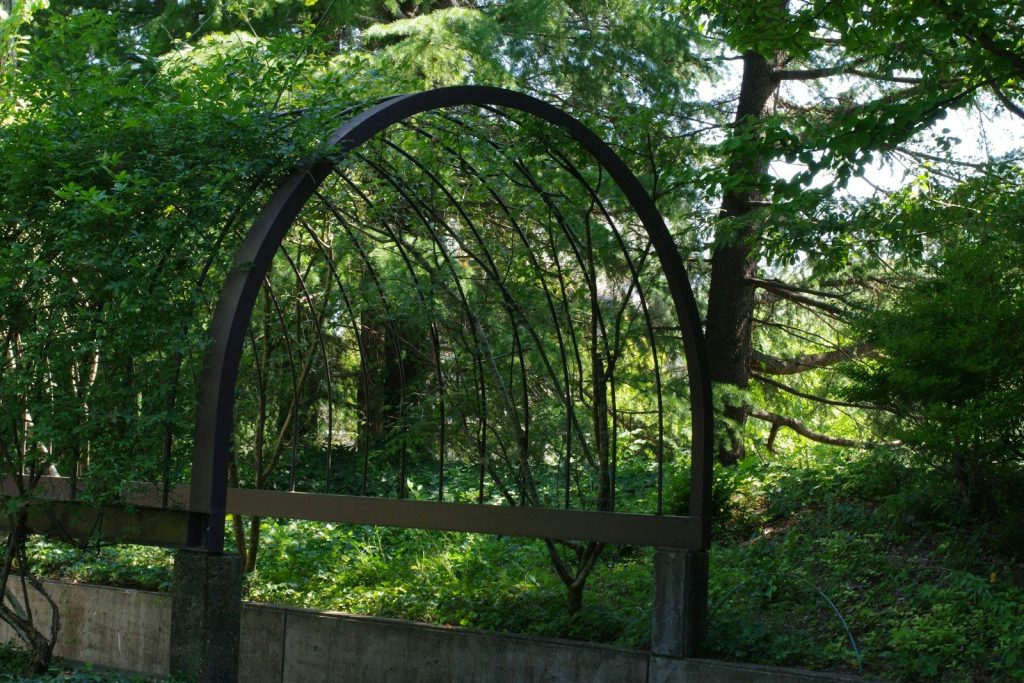 A metal arch sitting next to a lush green forest