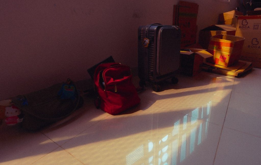 Red backpack and other bags on a sunlit floor.