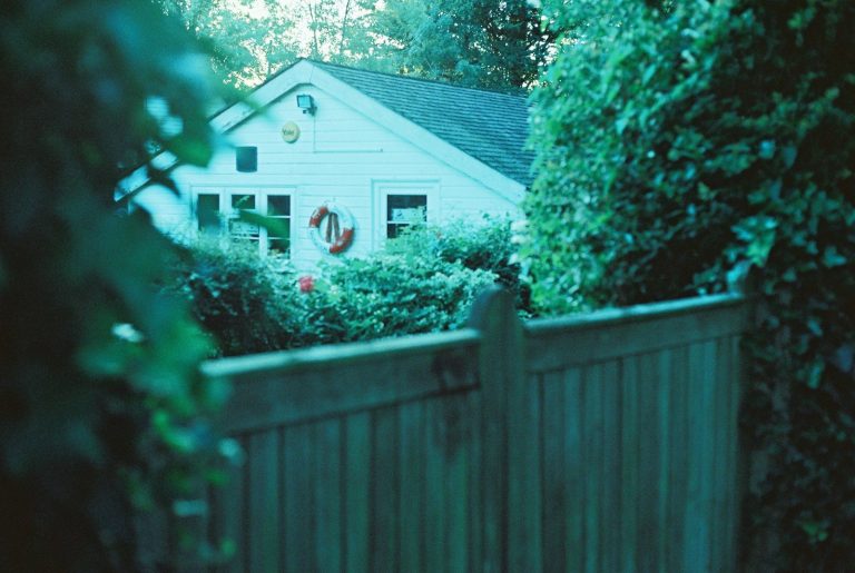 White house behind wooden fence and green foliage