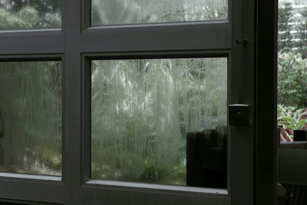 Rain streaks on a window overlooking greenery
