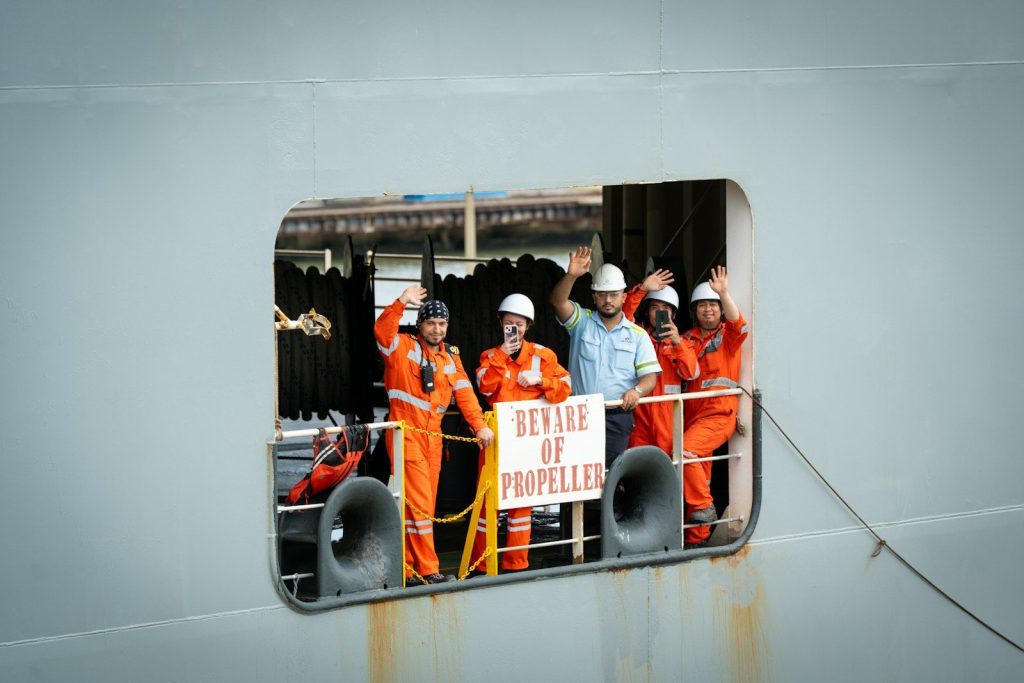 Crew members wave from a ship's opening.
