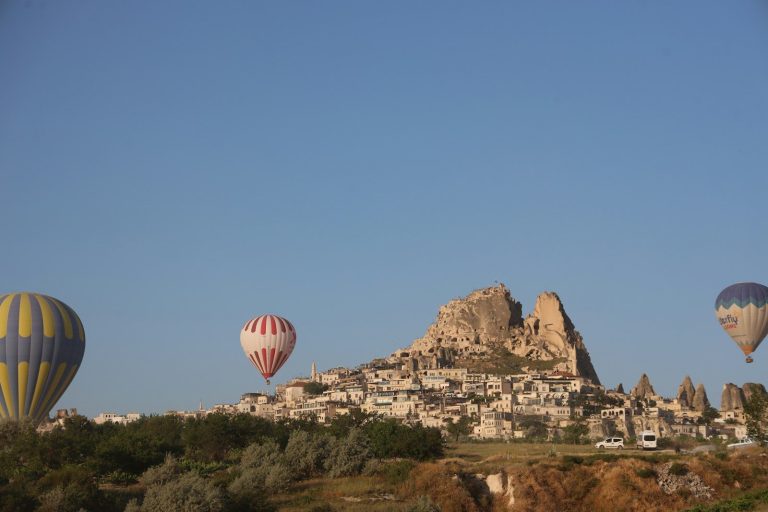 Hot air balloons fly over a unique rocky town.