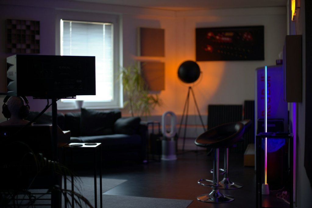 Dimly lit room with sofa, bar stool, and colorful lights.