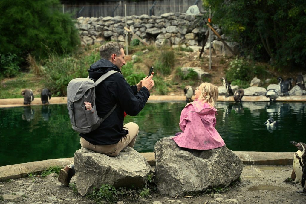 A man photographs his daughter near penguins.