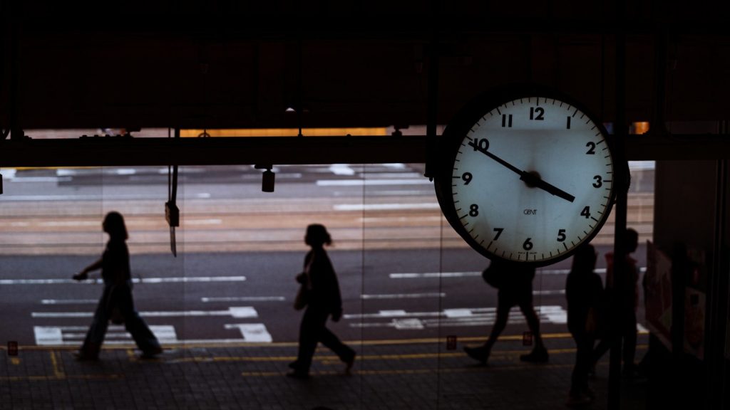 People walk past a large clock at night.